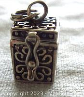 Front view of the rectangular silver prayer box charm showing detailed scrollwork with dots, the figure eight clasp, and attachment ring on top.