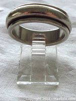 Front view of silver ring showing outer band and movable center band mounted on transparent ring stand.