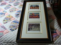 Overall framed set of three Tom Thomson numbered prints, showing the full black frame with gold trim and white mat with gold borders around individual prints.