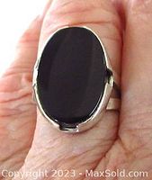 Top view of oval black onyx stone set in silver ring on finger, showing smooth surface and bezel setting.