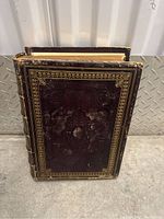Front cover of the large 1800s Bible showing dark brown worn leather with embossed floral design and gold border.