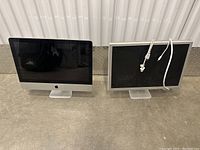 Two Apple iMac desktop computers side by side, one with cables wrapped on screen, other cable-free.