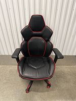 Front view of black gaming chair with red trim, showing seat, backrest, armrests, and caster wheels.