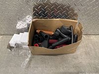 Box of mixed e-bike handlebar grips and parts seen from above, showing multiple black and red grips, with some brown grip and rolled black strip.