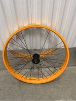 Yellow rear rim with black spokes and hub, no tire mounted, leaning on metal barrier.