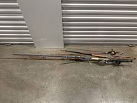Multiple fishing rods with some fitted with reels laid on concrete floor