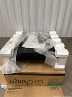 Harman Kardon FL 8300 CD changer unit on top of its original box with protective foam packaging and documents on top.