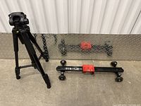 Full view of the black tripod and black Kamerar dolly slider with a red mounting plate on a metallic platform.