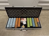 Aluminum carrying case open showing rows of poker chips in different colors, two decks of playing cards, dealer button, and a dice shaker with dice inside.