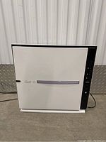 Front view of white air purifier unit on concrete floor, showing front panel and side control panel