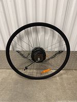 Full view of black rear wheel rim with metal spokes, Shimano cassette, and integrated motor hub. Shows approximate size and mounted reflector.
