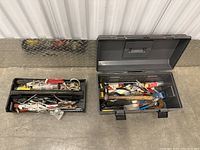 Two black toolboxes opened showing assorted hand tools inside including saw, pliers, hammers, caulking gun, electric drill, screwdrivers.