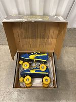 Open box showing vintage Puma roller skates inside with blue and yellow color scheme and yellow wheels.