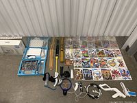 Wide shot showing Wii console with box, various controllers, accessories, and 21 Wii games laid out on floor