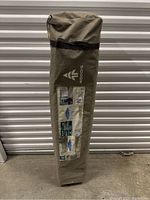 Packed Woods Big Top shelter frame in branded carrying bag leaning against storage wall.