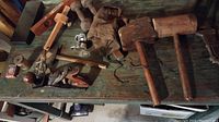 Collection of antique wooden and metal hand tools arranged on a worn green wooden surface, including mallets, hand planes, a glove, and adjustable wrench.