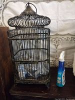 Front and side view of the large vintage metal birdcage next to a cleaning spray bottle for size reference.