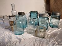 Collection of antique glass bottles and jars with clear and blue glass, some with metal lids and one with paper label.