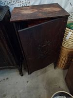 Front view of antique wooden cabinet with door ajar, showing wear and embossed detail