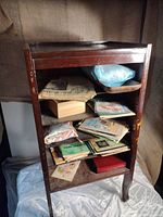Wooden cabinet with four shelves visible, containing a variety of papers and boxes, on a white fabric backdrop.