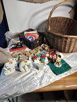 Wide view of large wicker basket with adjacent black basket holding Christmas cards, and various Christmas figurines and candle holders arranged in front.