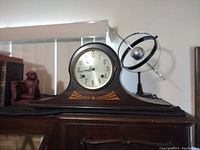 Photo of antique wooden mantel clock with inlaid design on top of cabinet.
