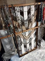 Photo showing a broad view of the handmade wooden rack with multiple necklaces hanging of various colors and styles including faux pearls and metal chains.
