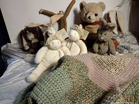 Six plush animals sitting on a bed with crocheted afghan in front.