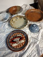 Full view of all six pottery items arranged on a white draped cloth showing different bowl shapes and the decorated plate with skeleton motif.
