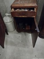 Side table with drawer open showing assorted costume jewelry and cabinet door open revealing small boxes and decorative items inside.