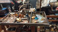 Photo of antique wooden tray with assorted vintage items arranged inside including bottles, barrels, keys, and figurines.
