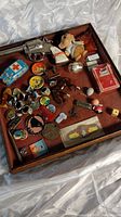 Full tray showing a variety of small vintage toys, rings, pins, and collectibles arranged on brown surface inside a wooden tray.