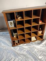 Photo showing both wooden trinket shelves with grid compartments, arranged at an angle on a fabric surface, displaying small items inside some compartments