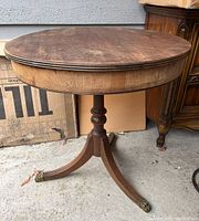 View of the entire antique round wooden table showing the top surface with visible scratches and the single pedestal base with three legs.