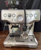 Front view showing control panel with power button, grind amount dial, filter size selection, pressure gauge, brew switches, steam wand and portafilter attached