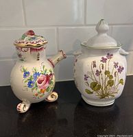 Photo of both porcelain pots on a dark countertop showing floral designs and condition.