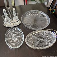 Five crystal and silver plated serveware pieces arranged on table. Includes large round platter, oval bowl, small oval dish, two cruets, and cruet carrier.