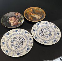 Overview of four decorative plates including two blue & white floral Johnson Brothers plates and two colored art plates by Norman Rockwell and M.J. Hummel