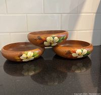 Three wooden bowls displayed on a countertop showing floral designs on the sides.