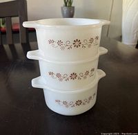 Three stacked white milk glass baking dishes with brown floral pattern on exterior and two short handles each