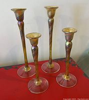 Four hand blown glass candle stick holders, two tall and two shorter, with iridescent gold spiral design on a red surface