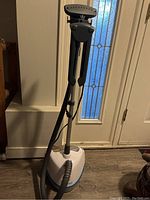 Full view of the Steamfast clothing steamer showing upright handle and base tank on floor.