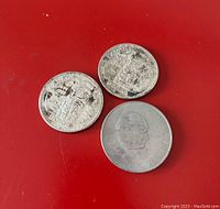 Three silver coins on a red surface: two Canadian silver dollars from 1966 with totem pole design and one vintage coin featuring Winston Churchill's profile.