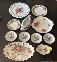 Overview photo showing multiple bird and floral china pieces on a dark surface. Pieces include various small plates, saucers, a gravy boat, and larger plates with floral and bird motifs.