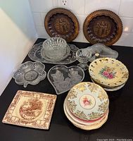 Full view of all plates and serveware on black countertop, showing decorative, crystal, and ceramic pieces with floral and embossed designs