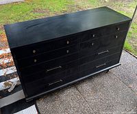 Full view of the dresser showing six drawers, black color, and mixed drawer handles. Minor surface damage visible.