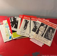 Photo showing a spread of 8 vintage O'Keefe Centre playbills on a red surface, displaying different front covers featuring performers and promotional artwork.