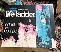 Top view of box packaging showing American La France Life Ladder instant fire escape with graphic of woman climbing ladder from window with fire below.