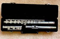 Opened black hard case showing the three separate pieces of Selmer Bundy II student flute inside lined foam interior.