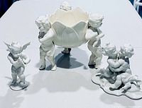 Five white porcelain cherub figurines and a cherub bowl arranged on a white surface showing all items in lot.